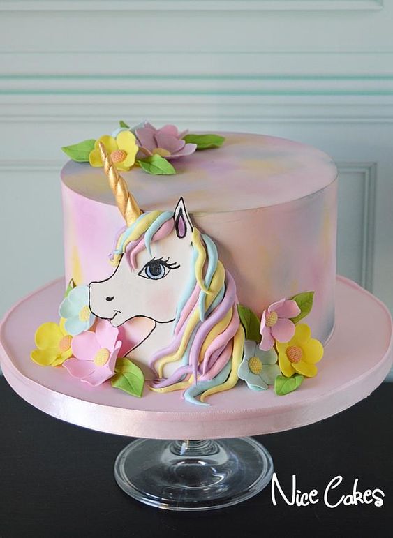 bolo com cobertura colorida e unicornio desenhado com enfeites de flores